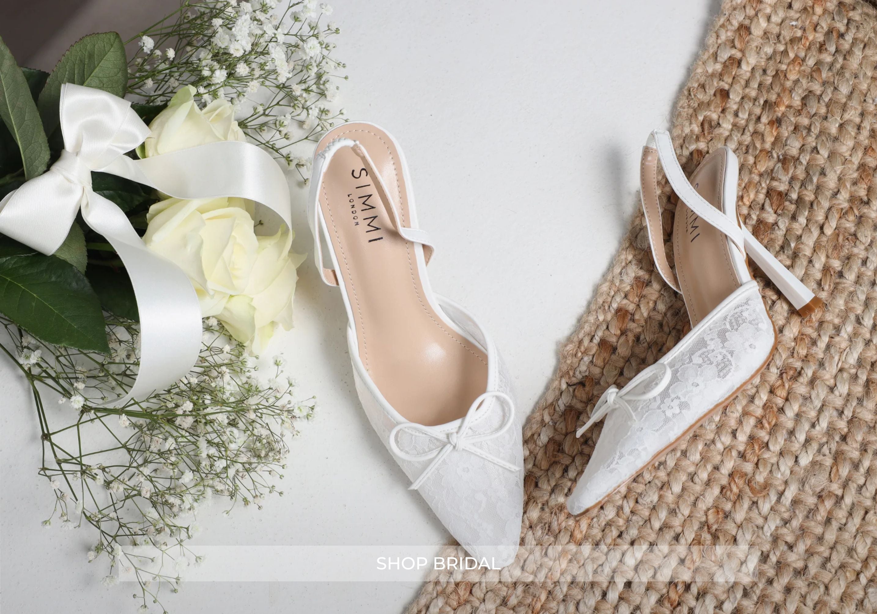 White bridal shoes with a bow on a textured surface with flowers in the background.