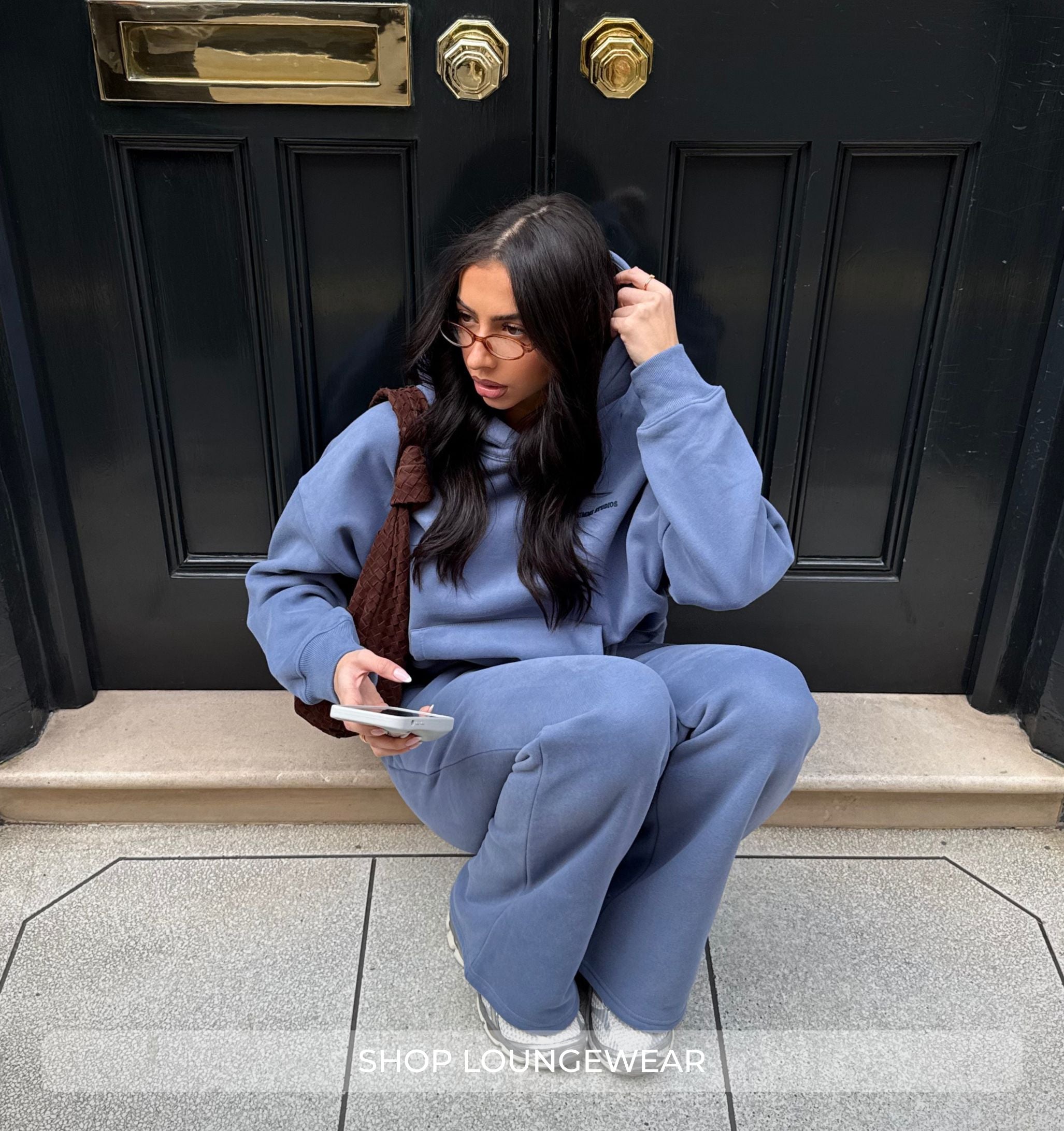 Person in blue tracksuit sitting on a step in front of a black door.