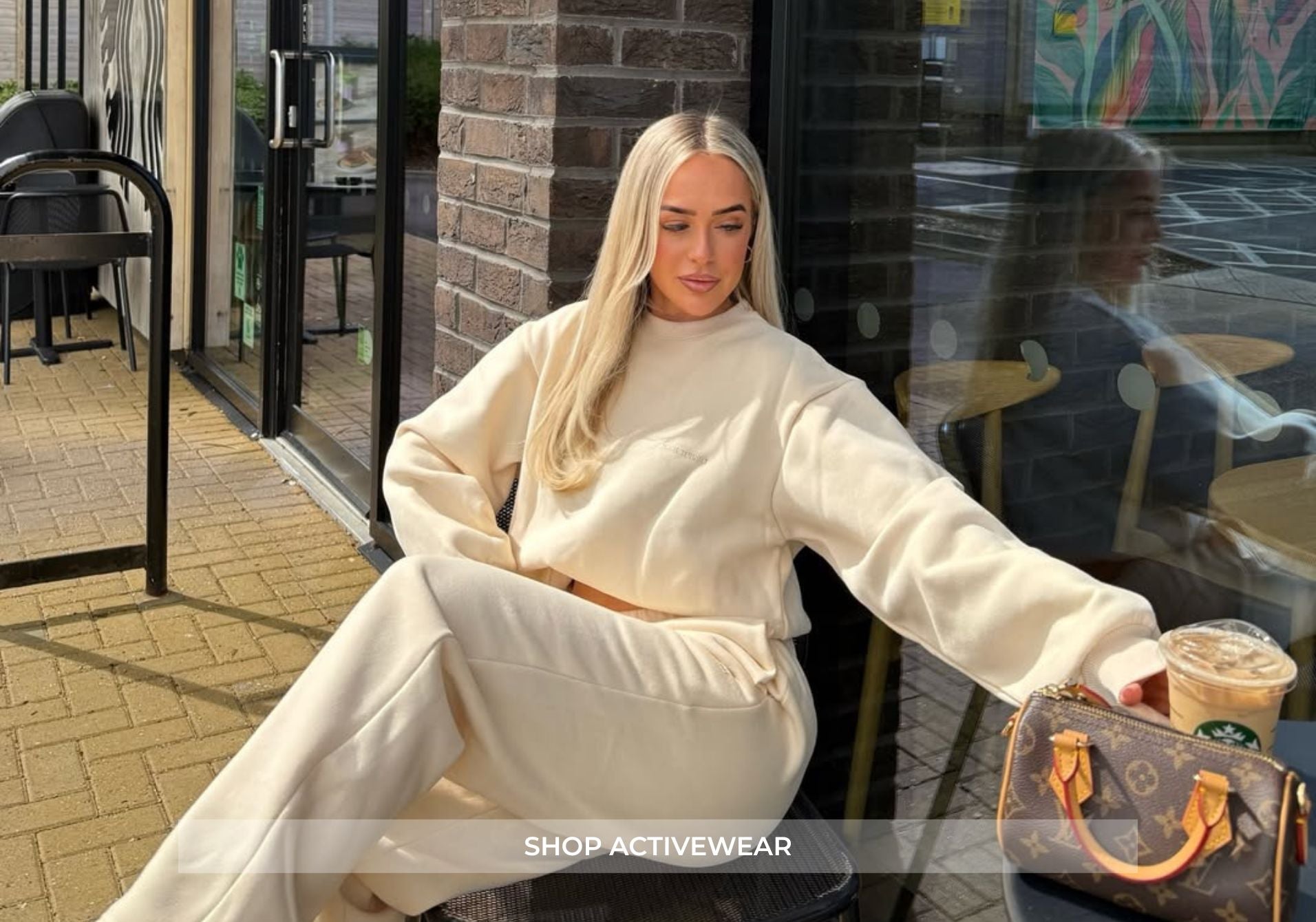 Woman in white outfit sitting outdoors with a handbag and coffee cup.
