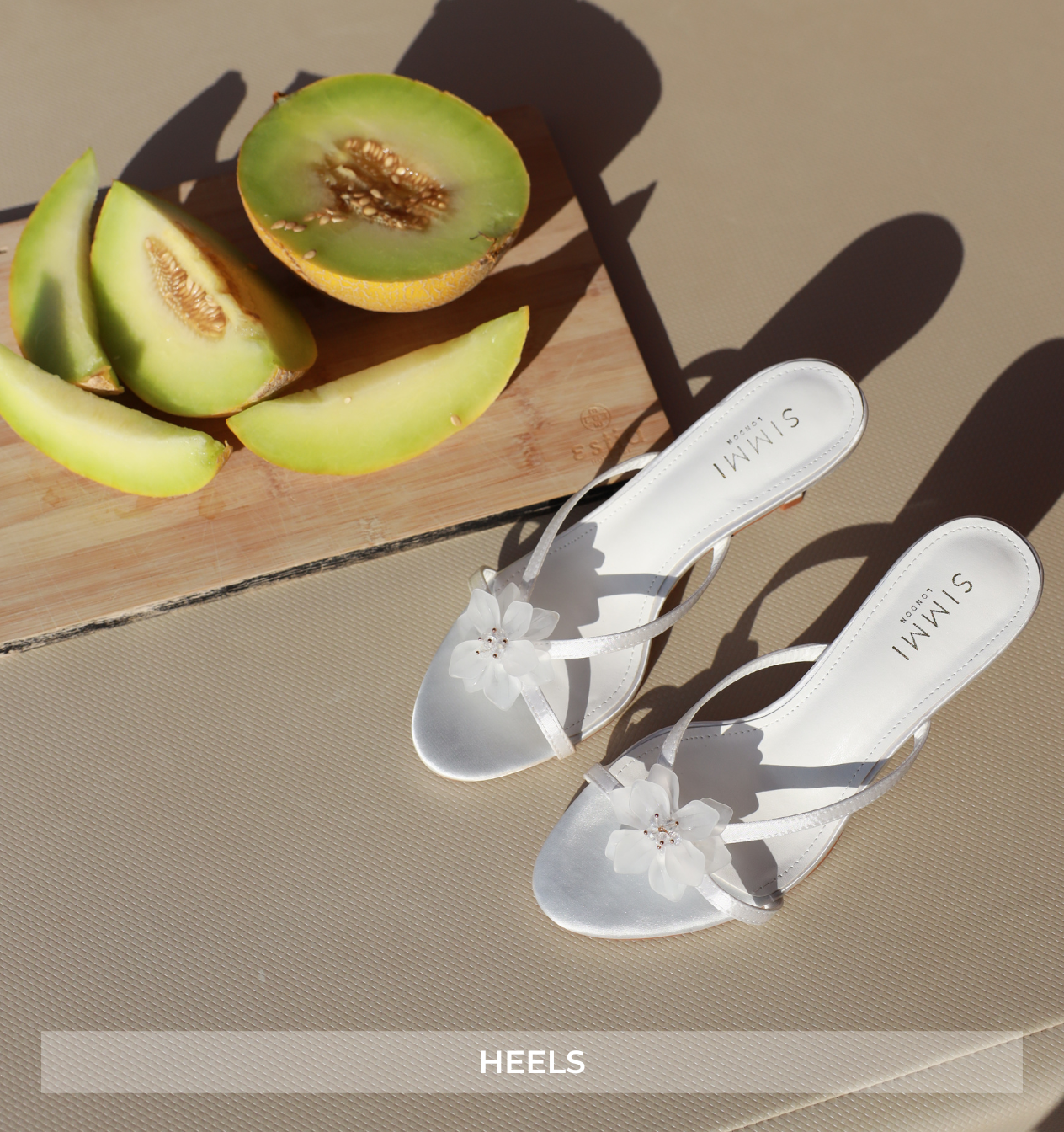 White sandals with floral details on a beige surface with sliced melons.