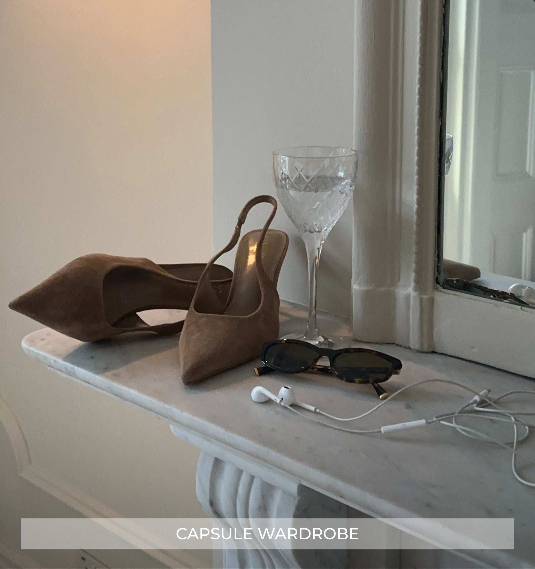 Brown suede shoes, sunglasses, and earphones on a marble surface with a glass in the background.
