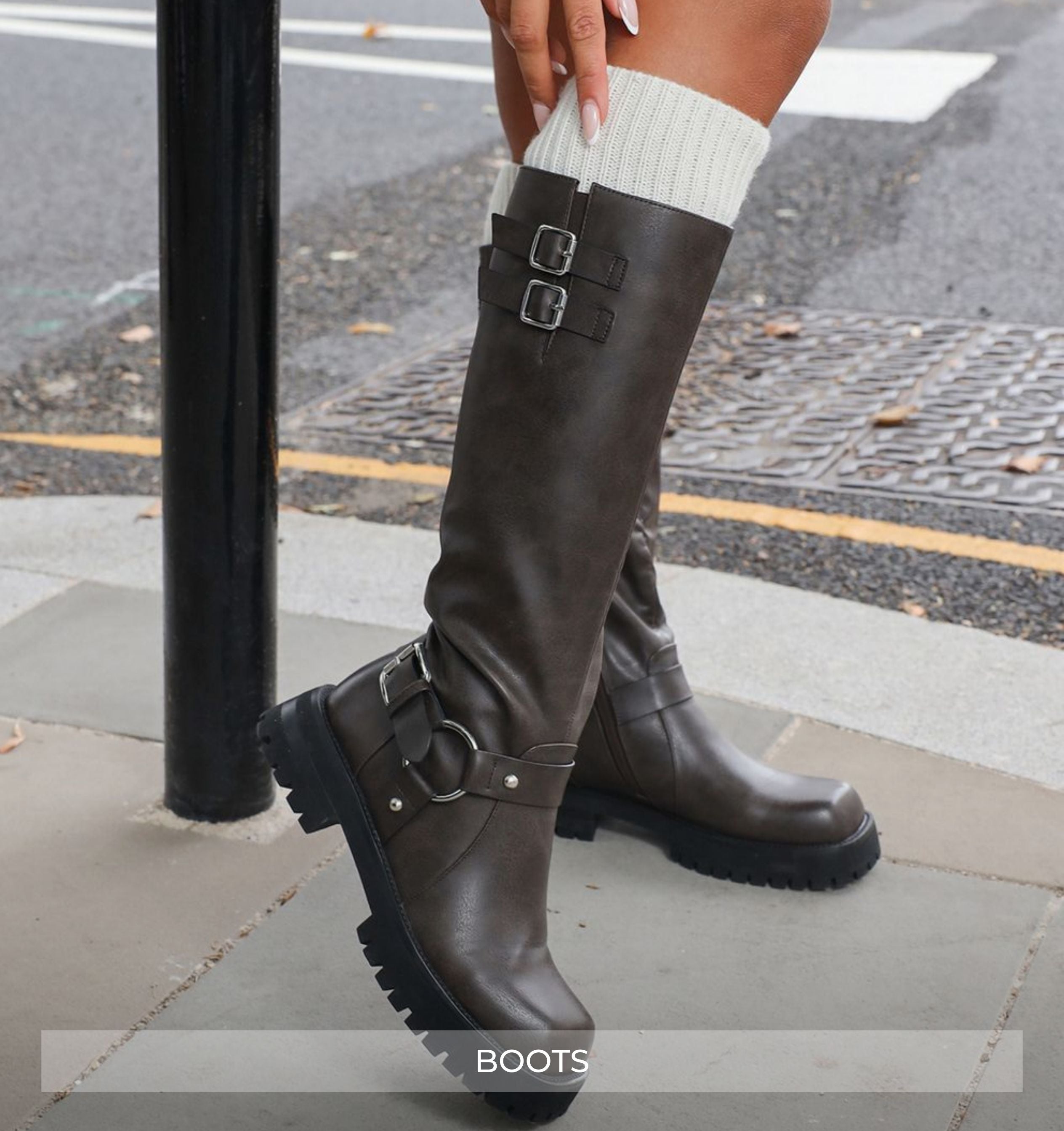 Brown knee-high boots with buckles worn by a person on a sidewalk.