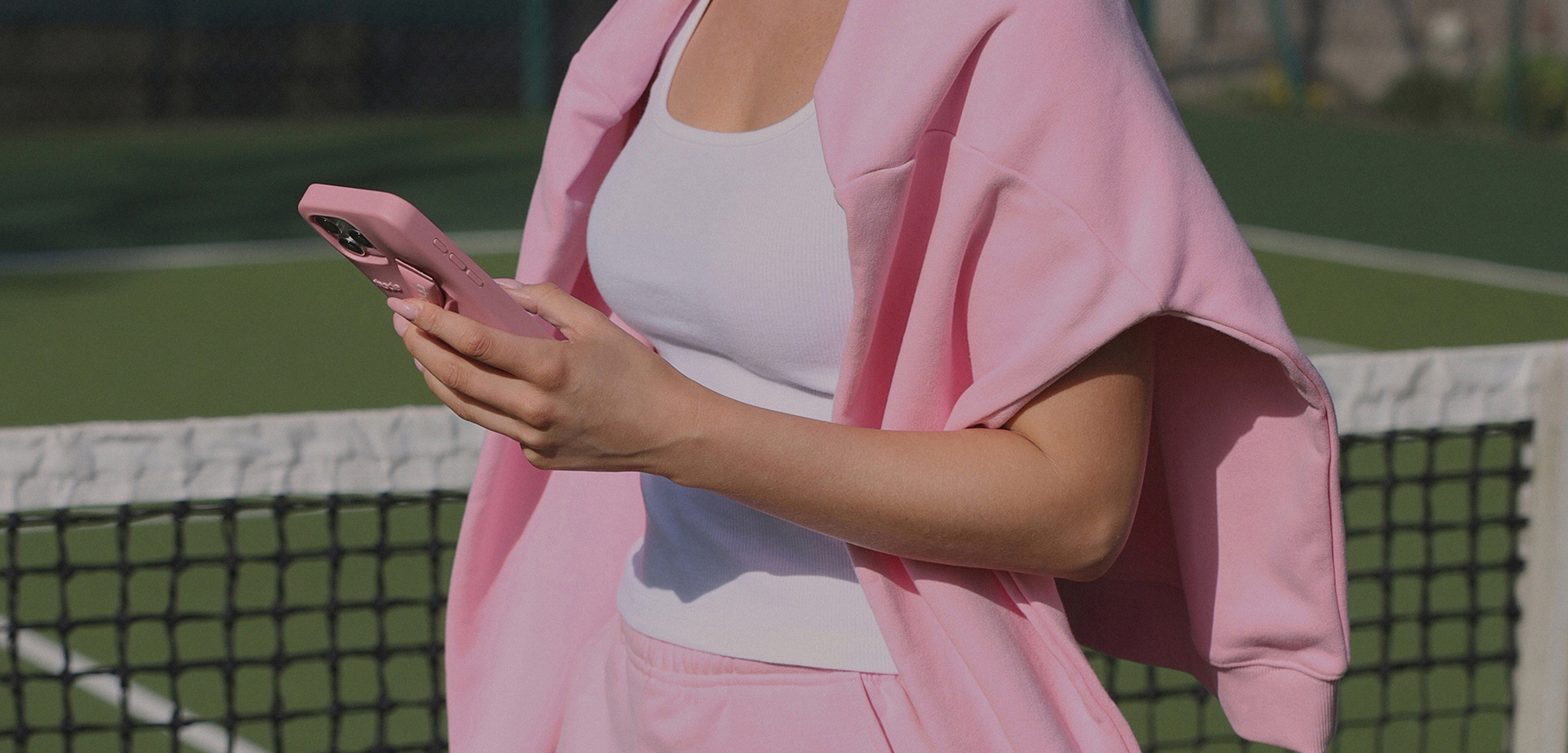 Person in pink jacket and white shirt using a phone on a tennis court