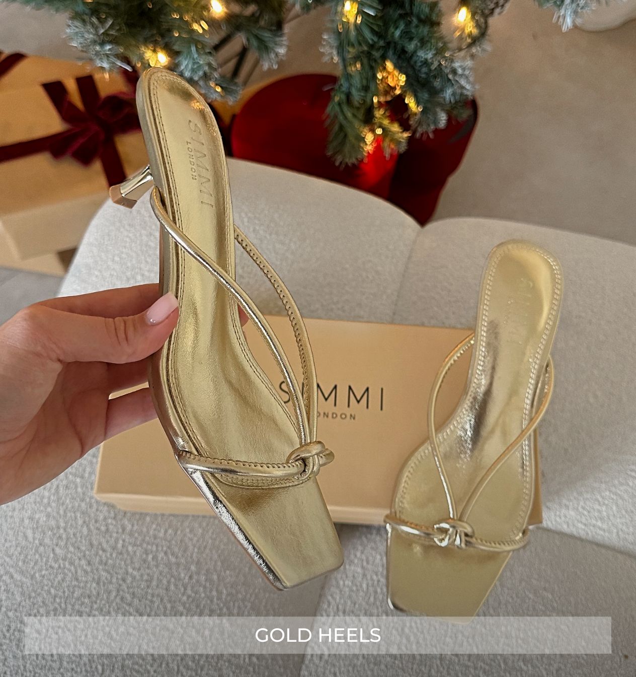 Gold high-heeled shoes held by a hand with 'Summi London' box in the background.