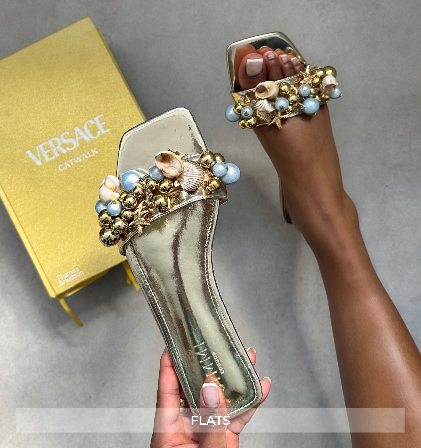 Versace embellished flats held by a hand with a Versace box in the background.