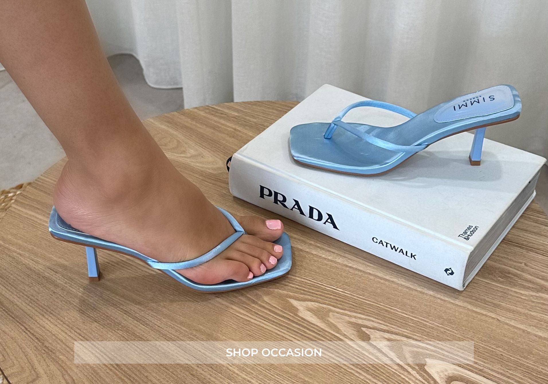 Blue high-heeled sandal on a Prada book with a wooden floor background