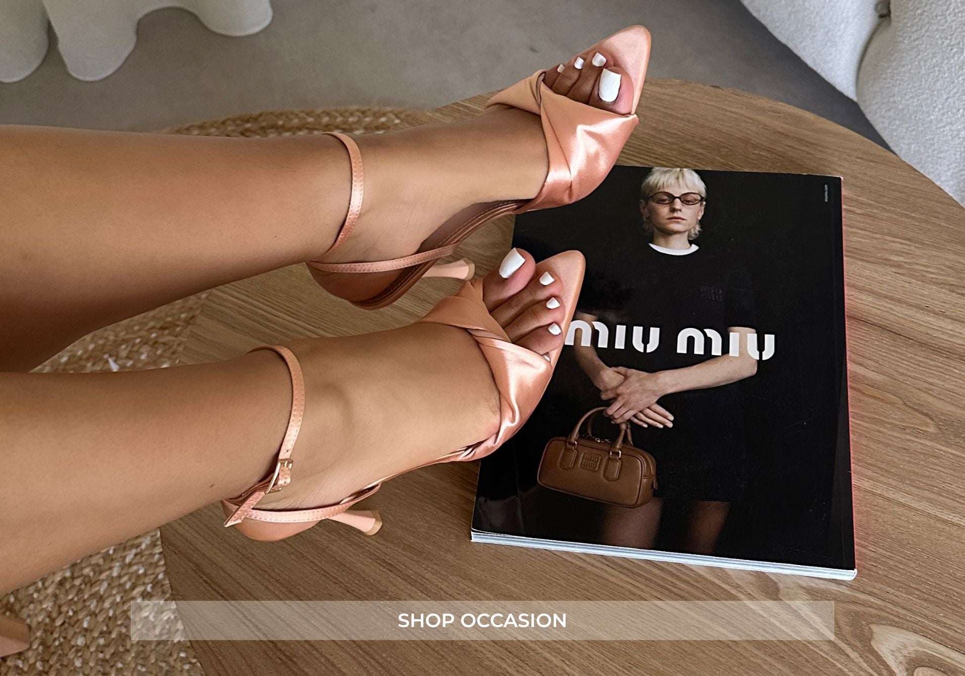 Person wearing pink high-heeled sandals with a Miu Miu magazine on a wooden table.