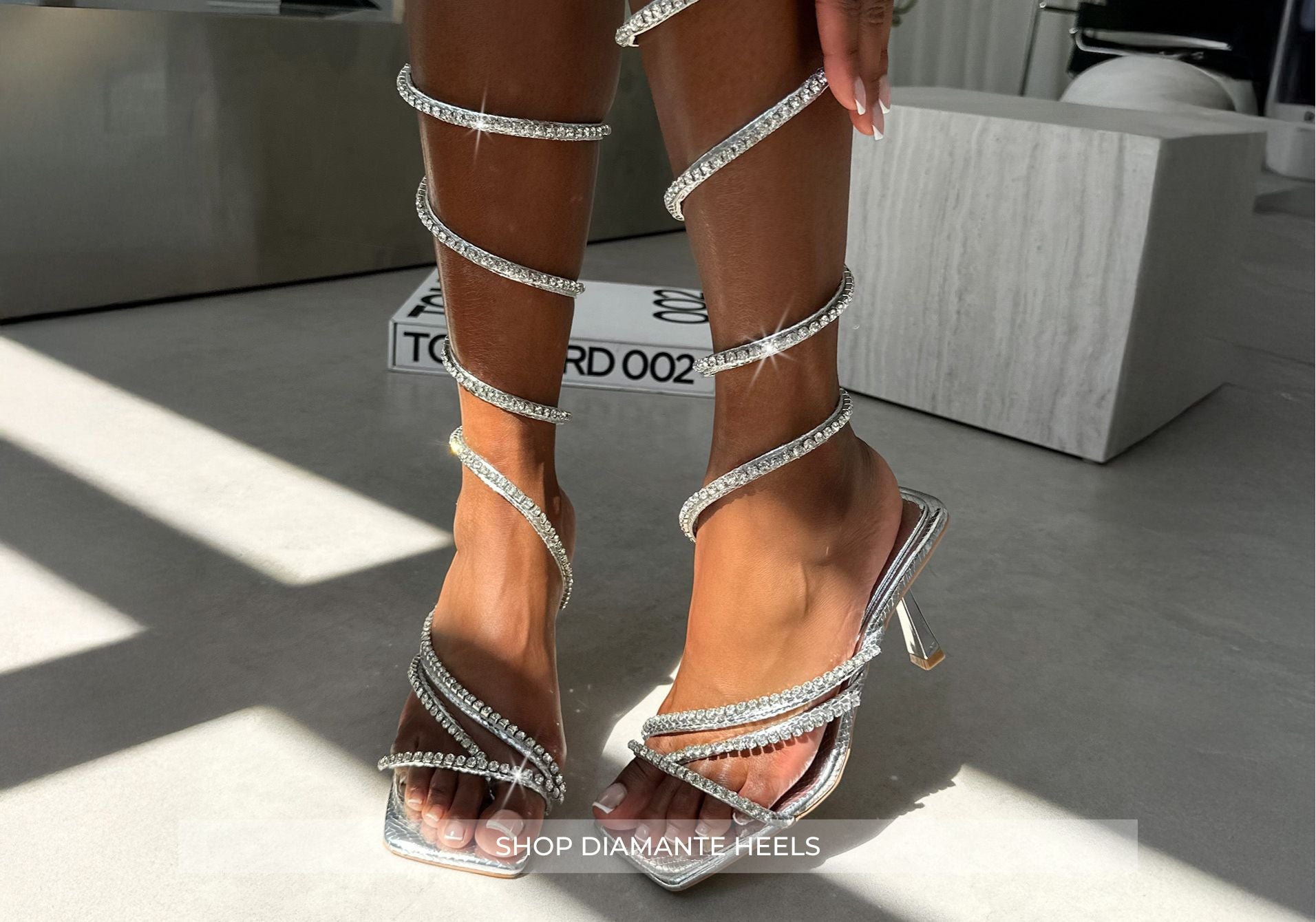 Silver strappy high-heeled shoes worn by a person indoors.