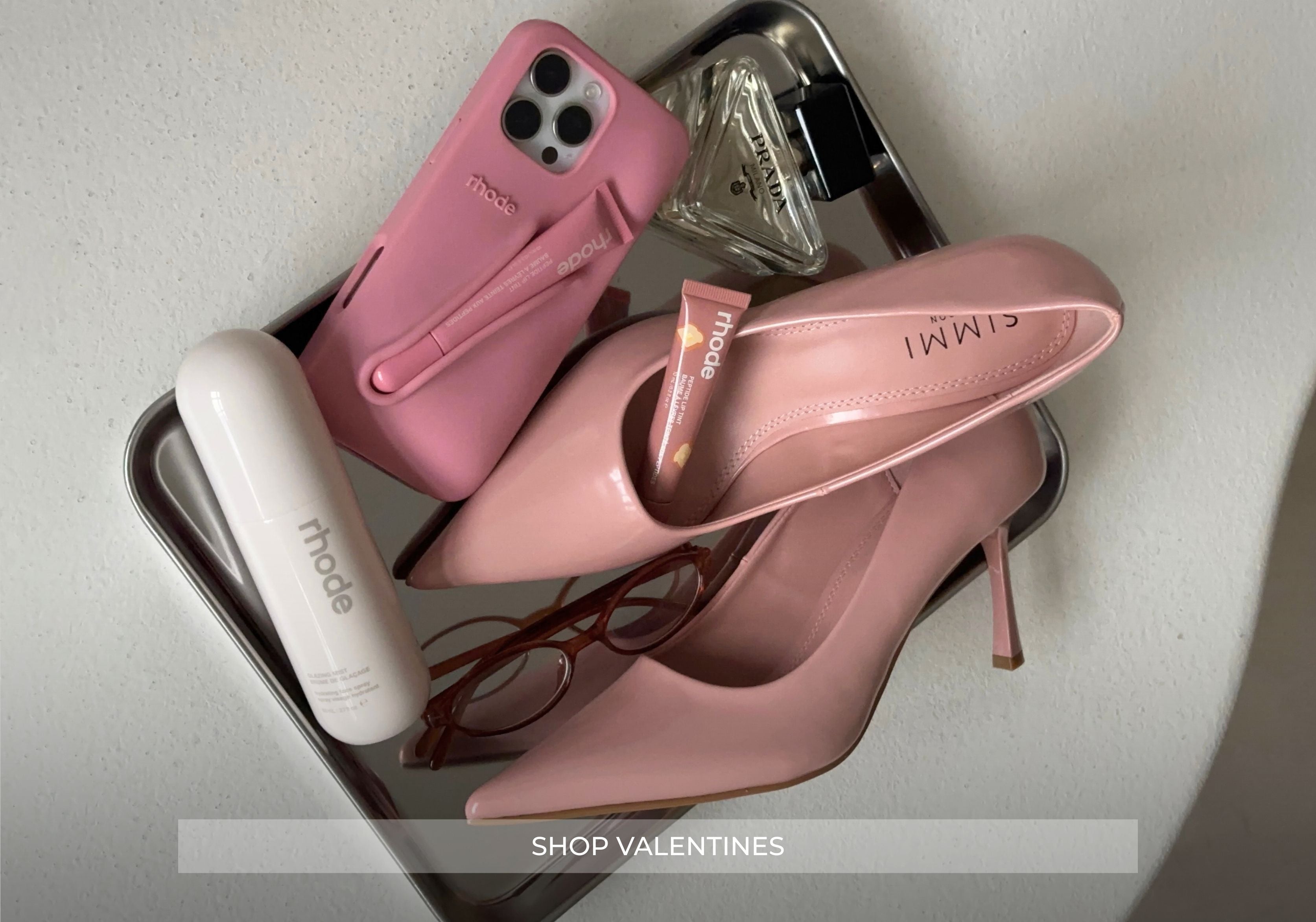Pink high heels, phone case, and lip gloss on a tray with 'Shop Valentines' text.