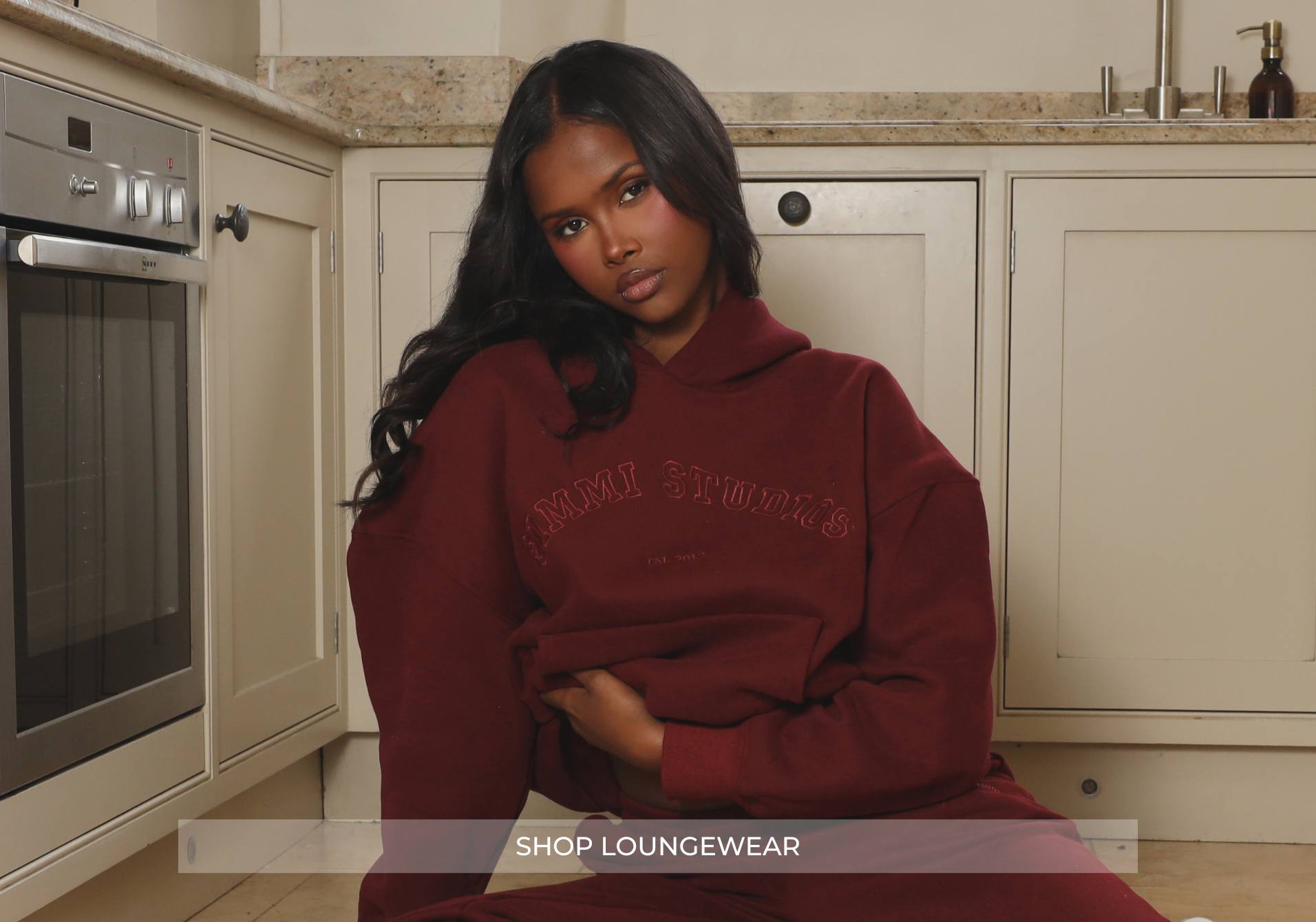 Woman in a red tracksuit sitting in a country kitchen with Simmi Studios on her hoodie. Shop Loungewear