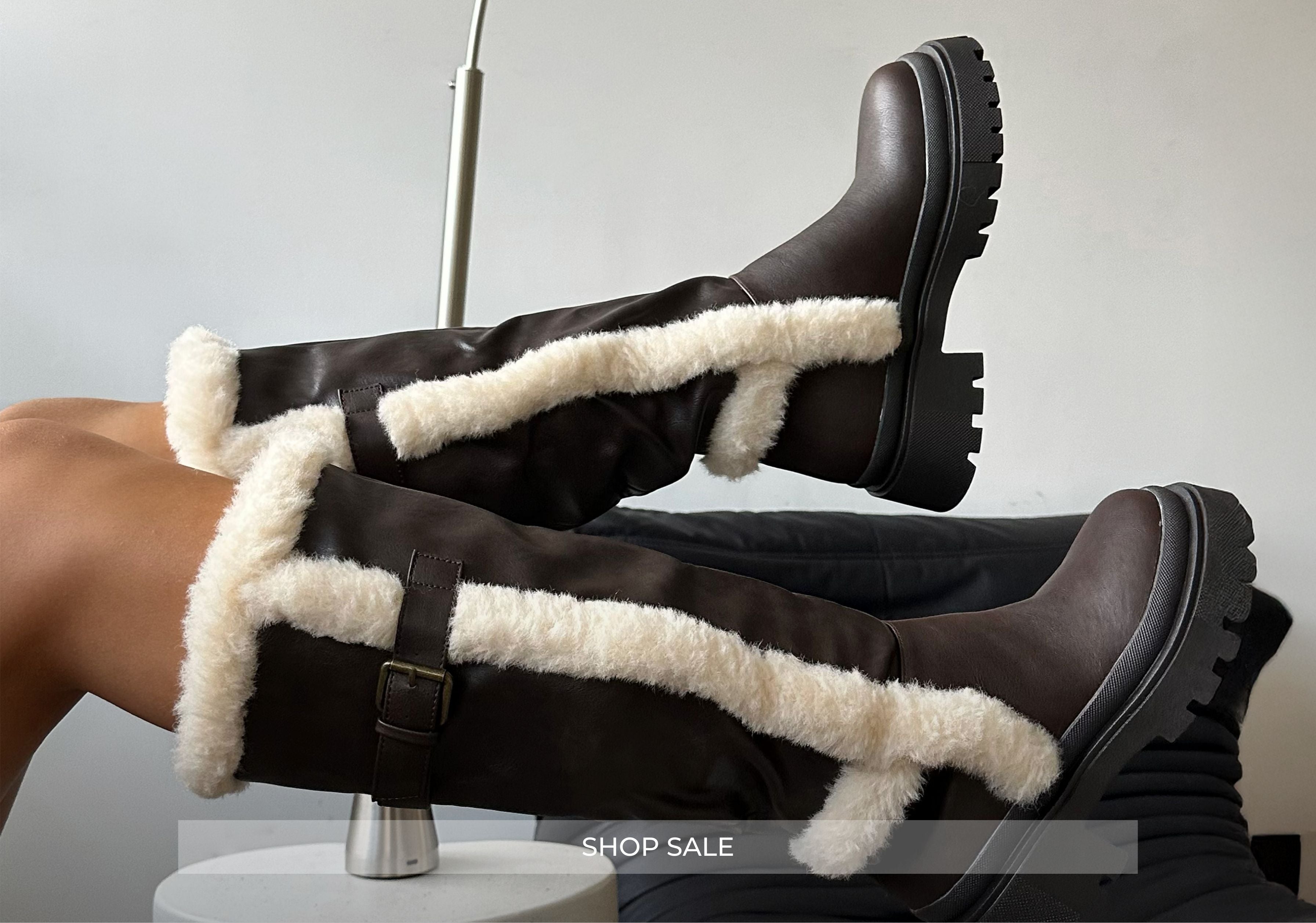 Brown knee-high boots with white fur lining on a gray background