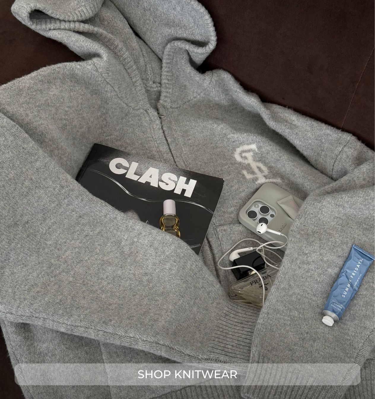 Gray knitwear with 'CLASH' branding and a phone inside, on a dark surface.