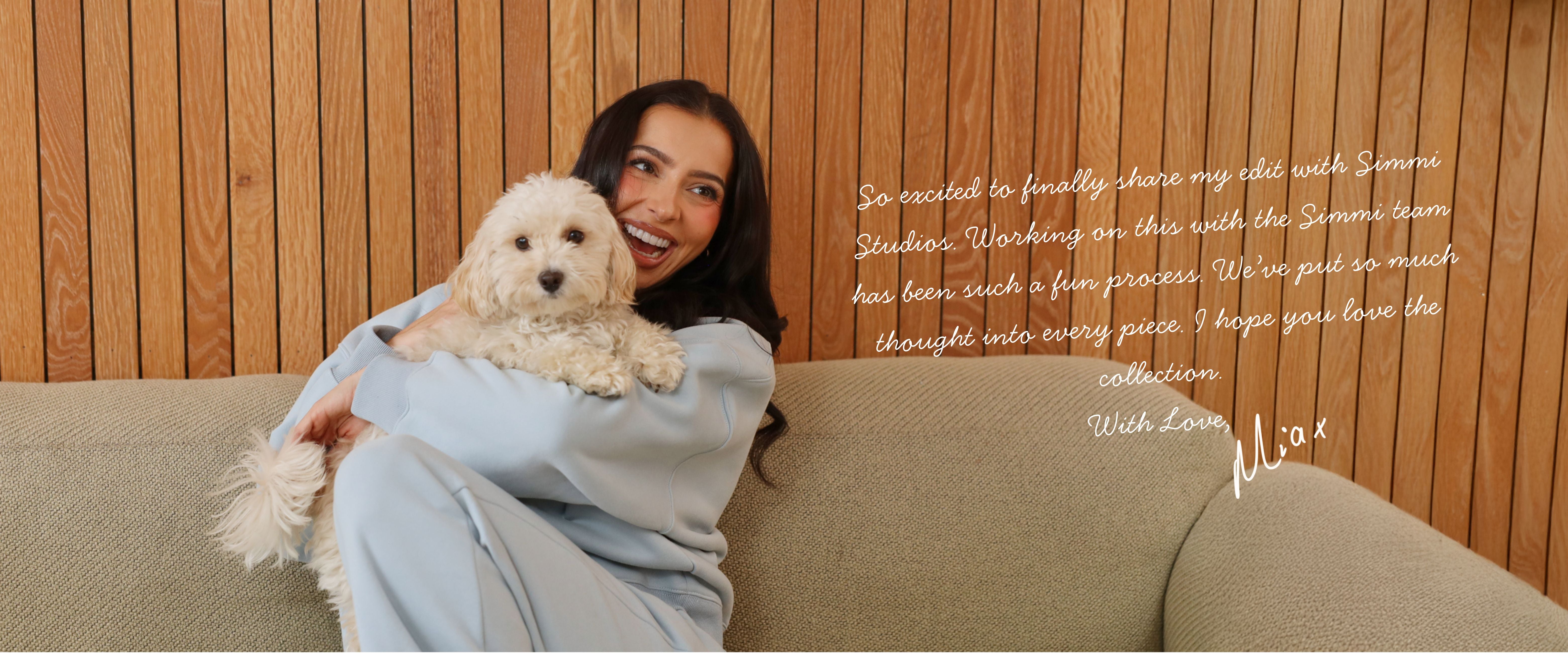 Woman holding a small white dog on a couch with a wooden wall background